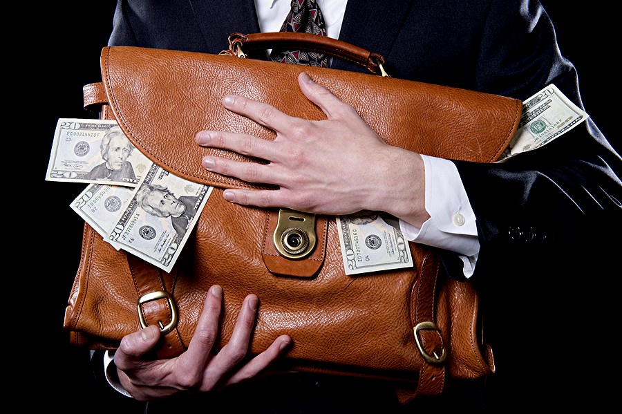 Closeup of man holding briefcase with money spilling out close to his chest